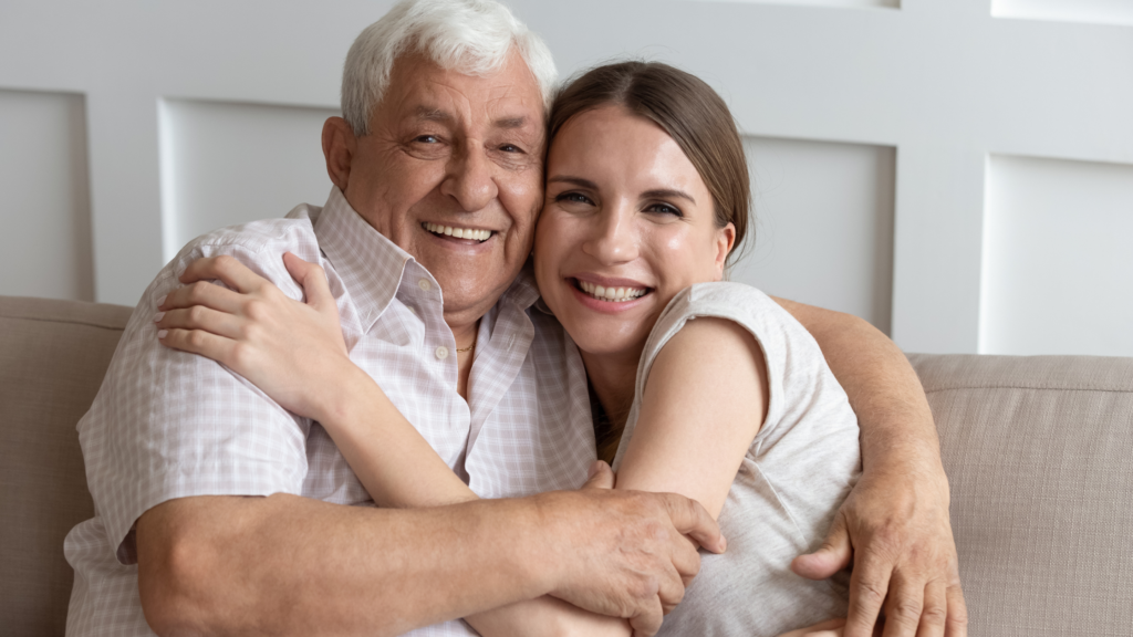 Adult daughter embracing her aging father on a couch showing emotional support during financial planning